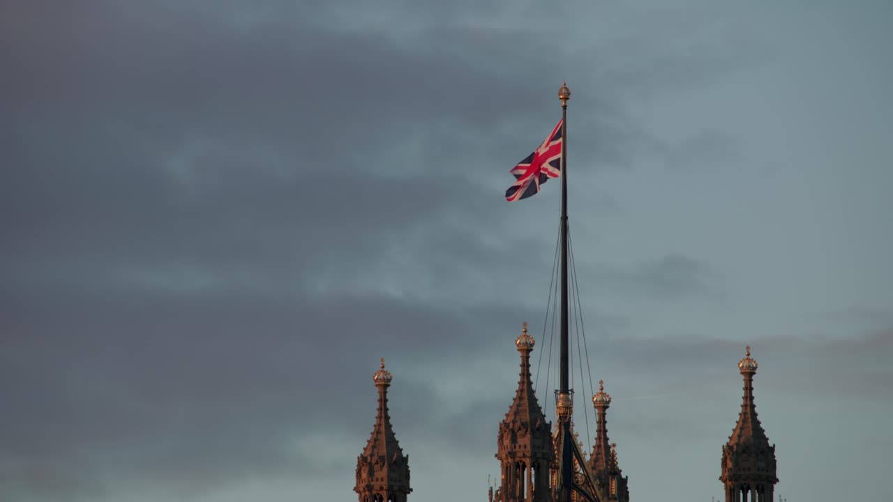 Tilt-up view captures the Gothic spires and crown-like pinnacles of Victoria Tower at Westminster, with the Union Jack fluttering against the evening sky in London