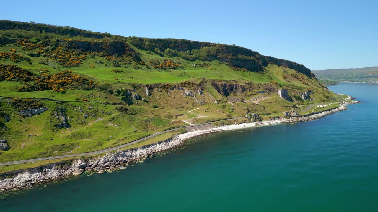 Side-on, reversing aerial video of the Causeway Coastal Route at Glenarm in County Antrim, Northern Ireland, UK on a bright and sunny day. Filmed in 4K, 60FPS and with Rec709 color.