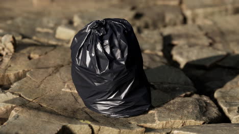 black trash bag lay on a rocky beach