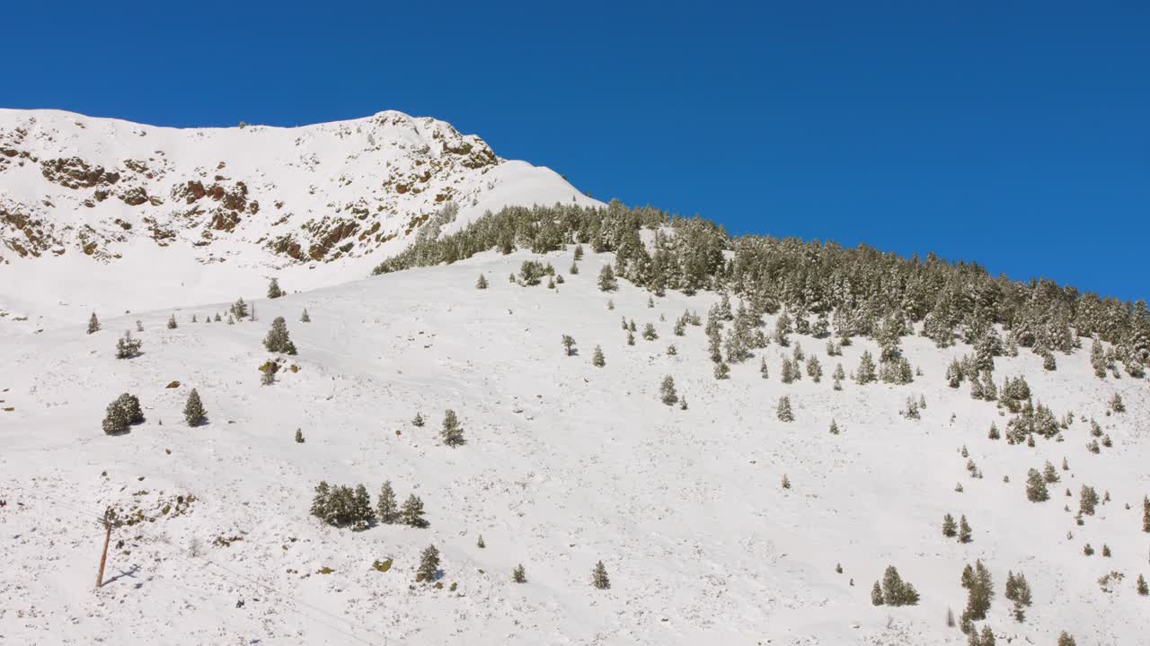An aerial view showcases a picturesque snowy landscape, featuring majestic mountains and a ski chairlift at a winter resort. The bright blue sky enhances the scene's serenity.