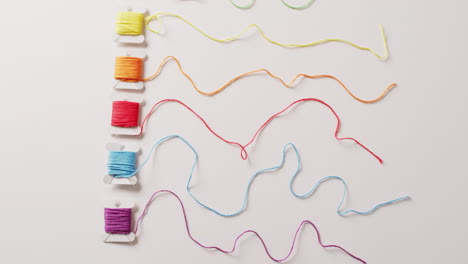 video of six bobbins of colourful embroidery threads unwound on white background