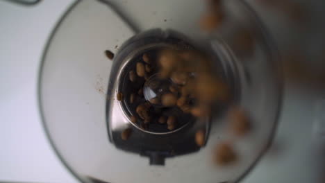 vista aérea de cerca en cámara lenta de granos de café marrones frescos esparcidos y vertidos en un elegante molinillo eléctrico para el café de la mañana