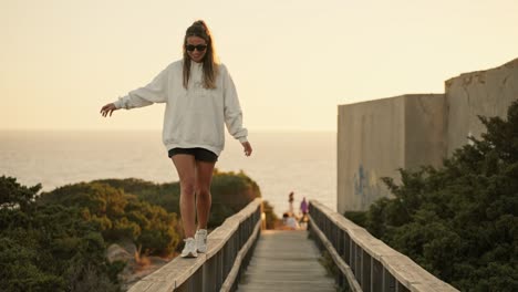 young woman having fun walking along a wooden railing at sunset