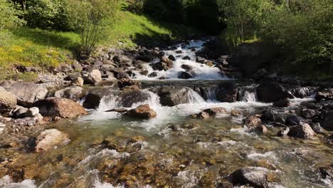 Clear-mountain-stream-flows-over-rocks,-creating-small-waterfalls-and-rapids-amidst-lush-greenery