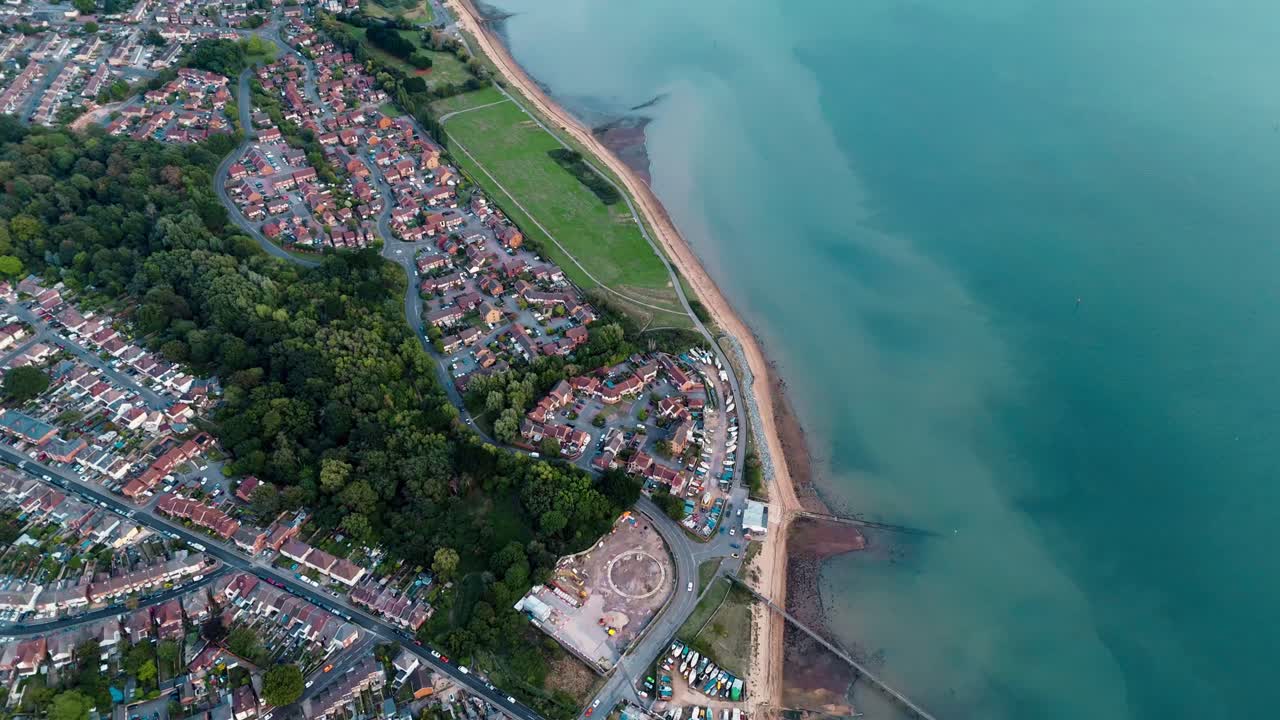 High-angle aerial drone view over Weston and Shore beach Southampton, showcasing sandy coastline, forest trees, and calm waters glowing in warm autumn sunset light