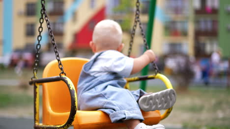 lovely baby boy sits on the yellow swing. cute kid turns around looking back. fun time at the playground. blurred backdrop.