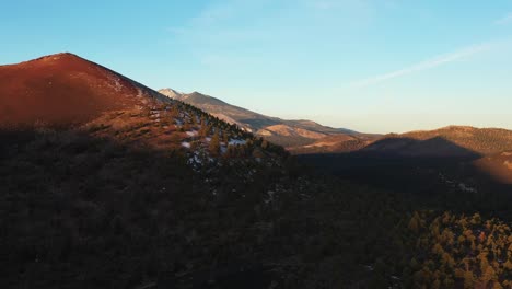 Aerial-shot-of-dawn-light-illuminating-Sunset-Crater-and-the-San-Francisco-Peaks,-northeast-of-Flagstaff,-Arizona,-as-seen-from-the-Coconino-National-Forest