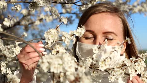beautiful girl in a medical mask stands near a flowering tree. coronavirus epidemic. covid-19