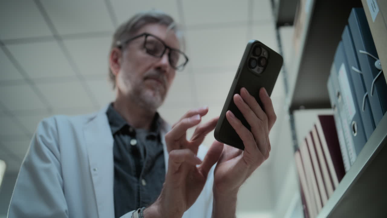 científico mayor usando un teléfono inteligente en una biblioteca