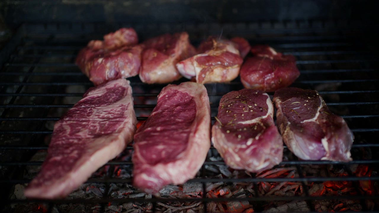Pezzi assortiti di carne cruda posizionati su una griglia sopra carboni ardenti prima della cottura.