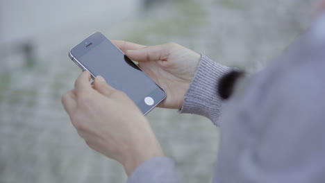 una foto cortada de una mujer usando un teléfono inteligente al aire libre.