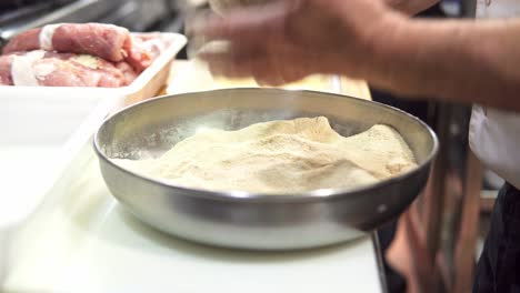 primer plano de un chef experimentado empanado bistecs y sumergiéndolos en huevo para freír