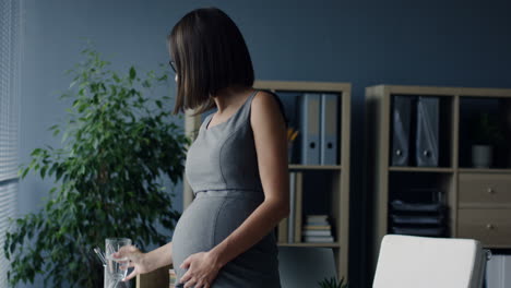 pregnant businesswoman having a headache and drinking water while standing in the office