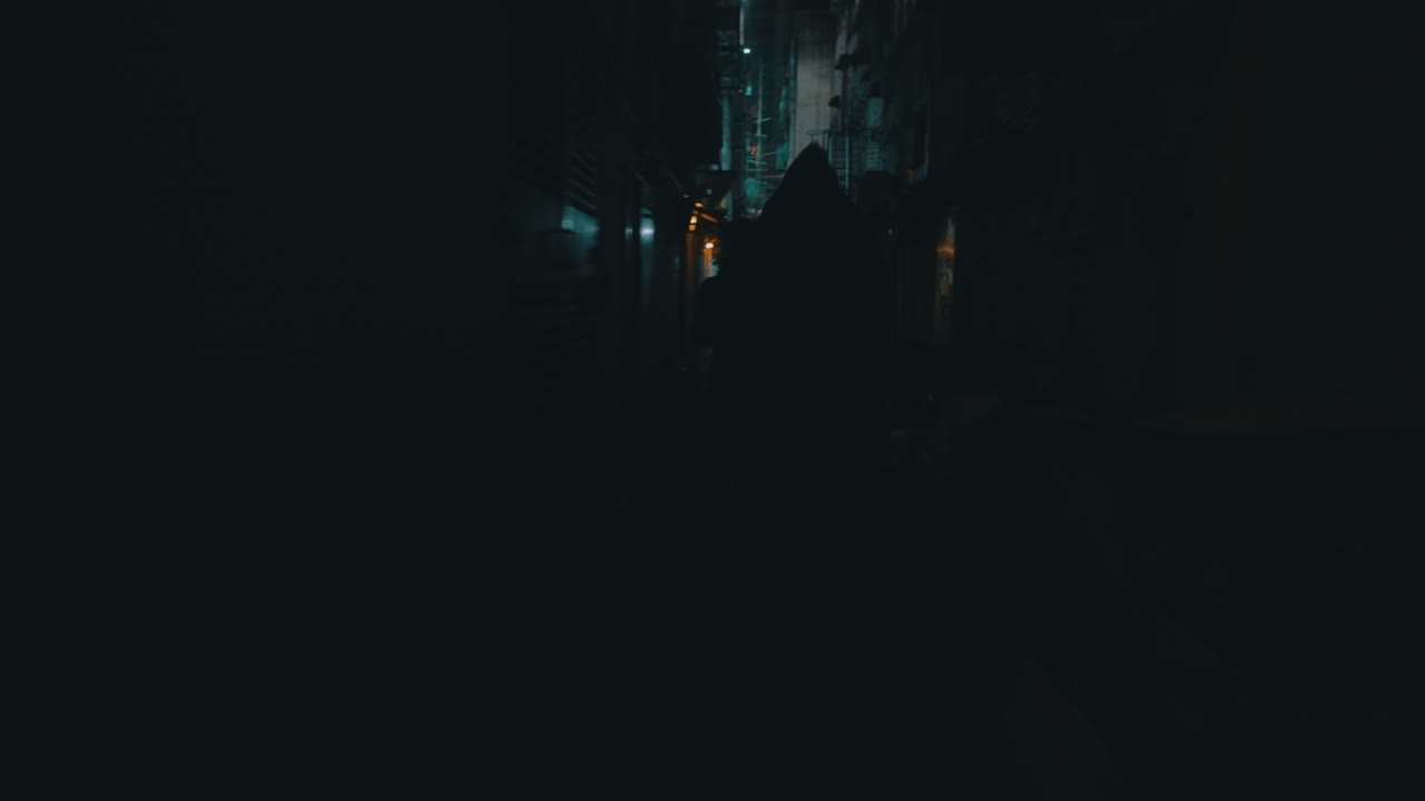 una toma cinematográfica de una figura encapuchada corriendo detrás de una chica en una calle pequeña, oscura, misteriosa y sucia durante la noche