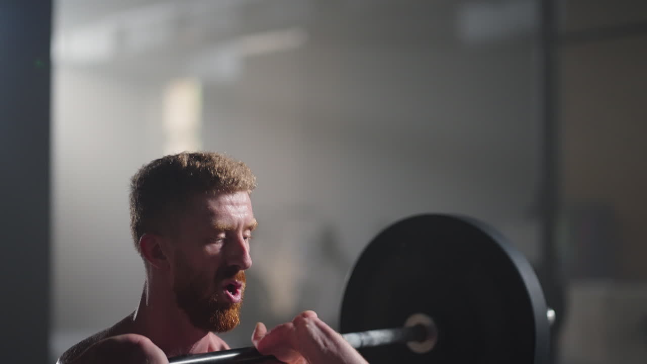Rallentatore: uomo fitness culturista si allena con un bilanciere, esercizi di sollevamento pesi, sportivo muscoloso che pratica powerlifting con pesi pesanti, esegue squat in palestra godendosi uno stile di vita sano.