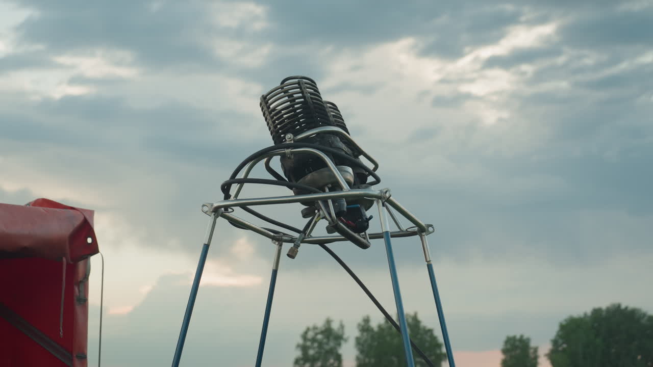 close up of twin burner assembly mounted on metal frame with blue support poles beside red trailer under cloudy sky, focus on intricate coil detail and precision setup for hot air balloon flight