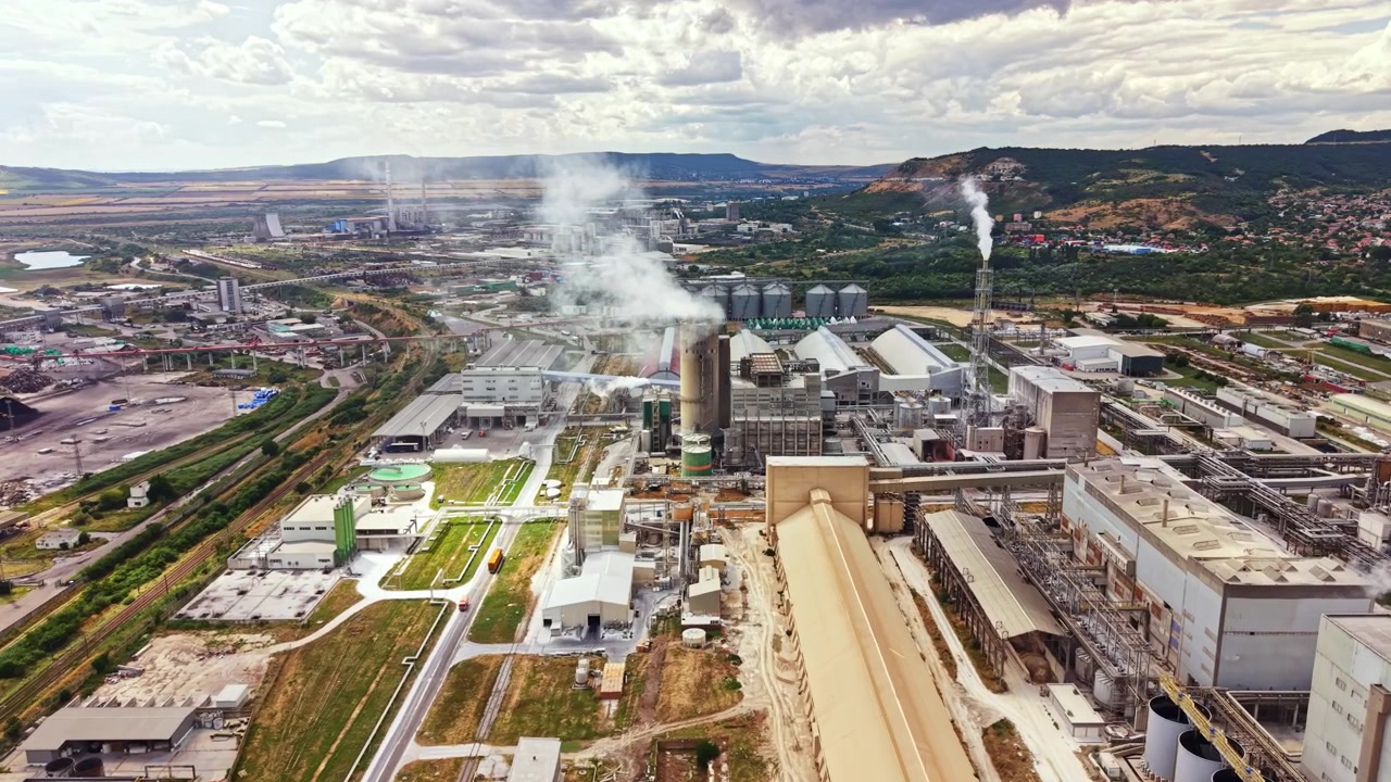 View of a large industrial complex with factories, smokestacks, and storage facilities in a rural area under a cloudy sky
