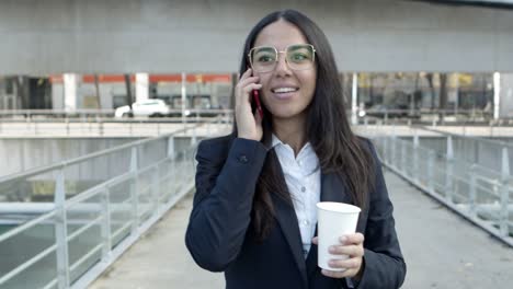 cheerful businesswoman talking by smartphone on street