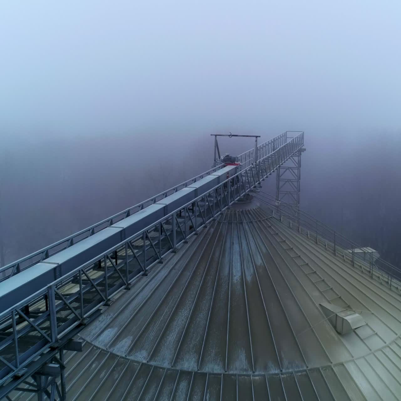 Rounded dirty top of a granary container. Drone footage along the beam leading to the tank top. Grey foggy weather backdrop