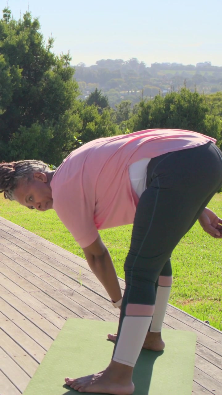 Vertical video: Stepping on green mat, senior lifting leg folding to warm on deck in pink with band