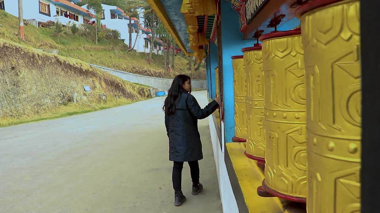 Tyttö pyörittää buddhalaisia uskonnollisia rukousmyllyjä luostarissa, kuvattuna matalasta kuvakulmasta Bomdilan luostarissa, Arunachal Pradeshissa, Intiassa.