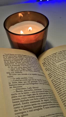 vertical shot of a book open with a lit candle beside it