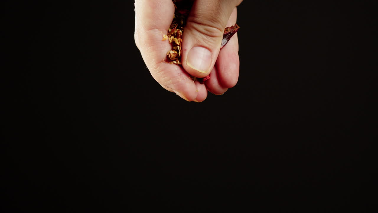 Close-up of Hand Sprinkling Dried Spices on Black Background