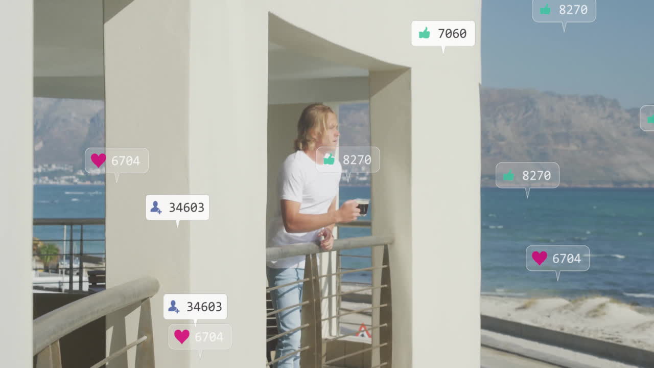 Animation of media icons over caucasian man with cup of coffee at seaside