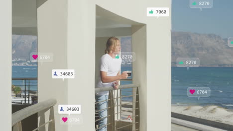 animation of media icons over caucasian man with cup of coffee at seaside