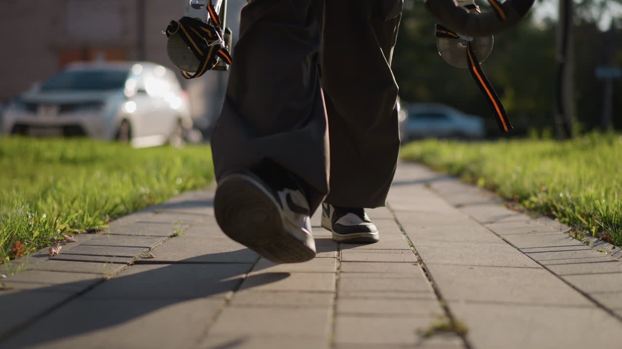 가운 회색 포장 된 보행길에서 는 다리의 클로즈업, 느슨한 어두운 바지와 색 발바닥의 어두운 스니커를 입고, 움직임에 초점을 맞추기 위해 흐릿한 배경