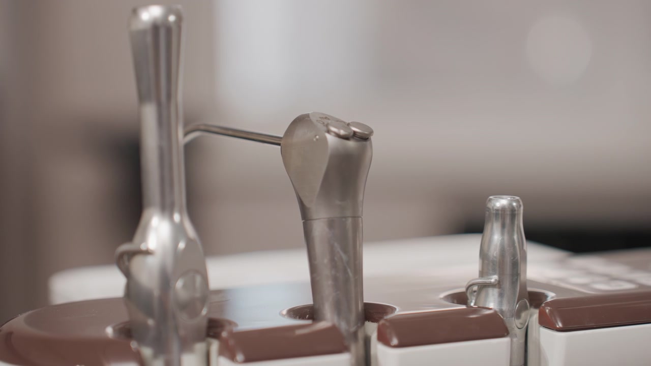 Close up of metal dental handpieces in stationary position on orthodontic device. shiny tools rest against brown and white plastic holders with soft lighting creating gentle reflections