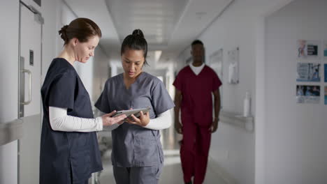 diverse female doctors discussing work, using tablet in corridor at hospital, slow motion