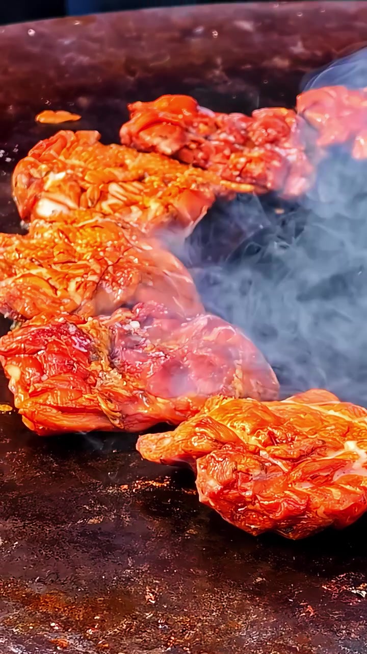 Rekaman vertikal close-up gerak lambat daging marinasi pedas mendesis di wajan panas dengan asap mengepul di kedai makanan jalanan