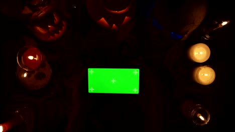 hombre juega un juego en un teléfono inteligente horizontal con pantalla verde en el fondo de la decoración de halloween