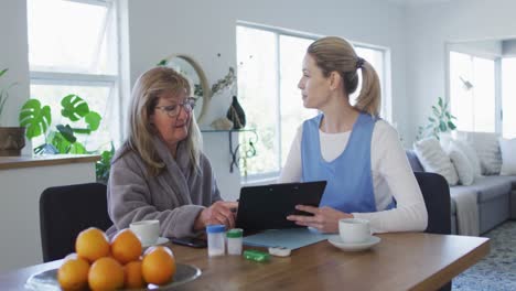 Trabajadora-De-Salud-Y-Mujer-Mayor-Discutiendo-Sobre-El-Portapapeles-En-Casa