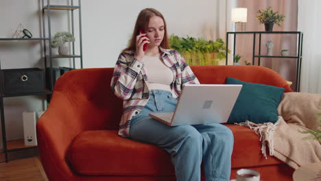 Young-woman-using-laptop-computer-sitting-on-sofa-working,-online-shopping-from-home-office