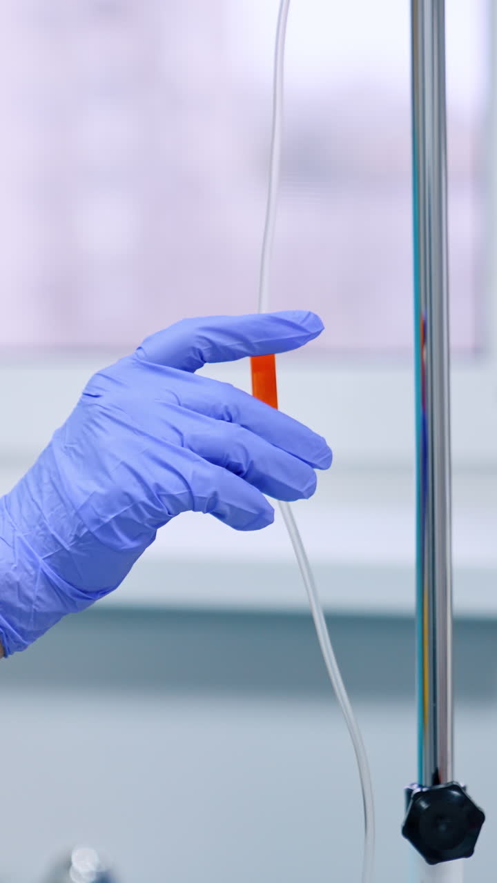 Unrecognized medical worker in blue latex gloves sets the drop counter. Nurse near the equipment in hospital ward. Vertical video