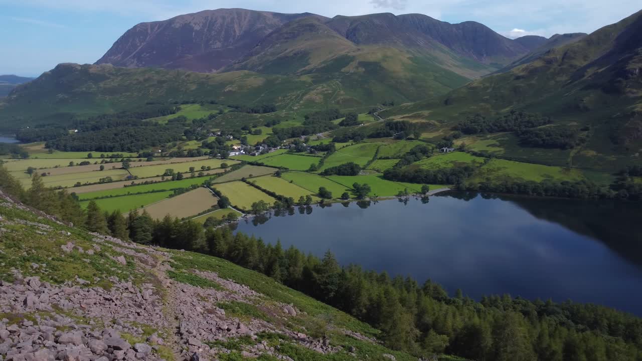 Smooth aerial video looking towards shores of Buttermere village and lake on beautiful summer's day - Lake District, UK