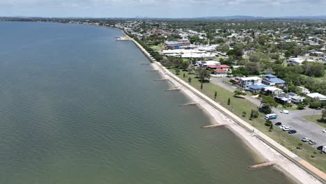 Drone-establishing-pull-away-shot-of-Brisbane-Brighton-Suburb,-camera-flying-over-water-Moreton-Bay-with-Brisbane-City-in-background