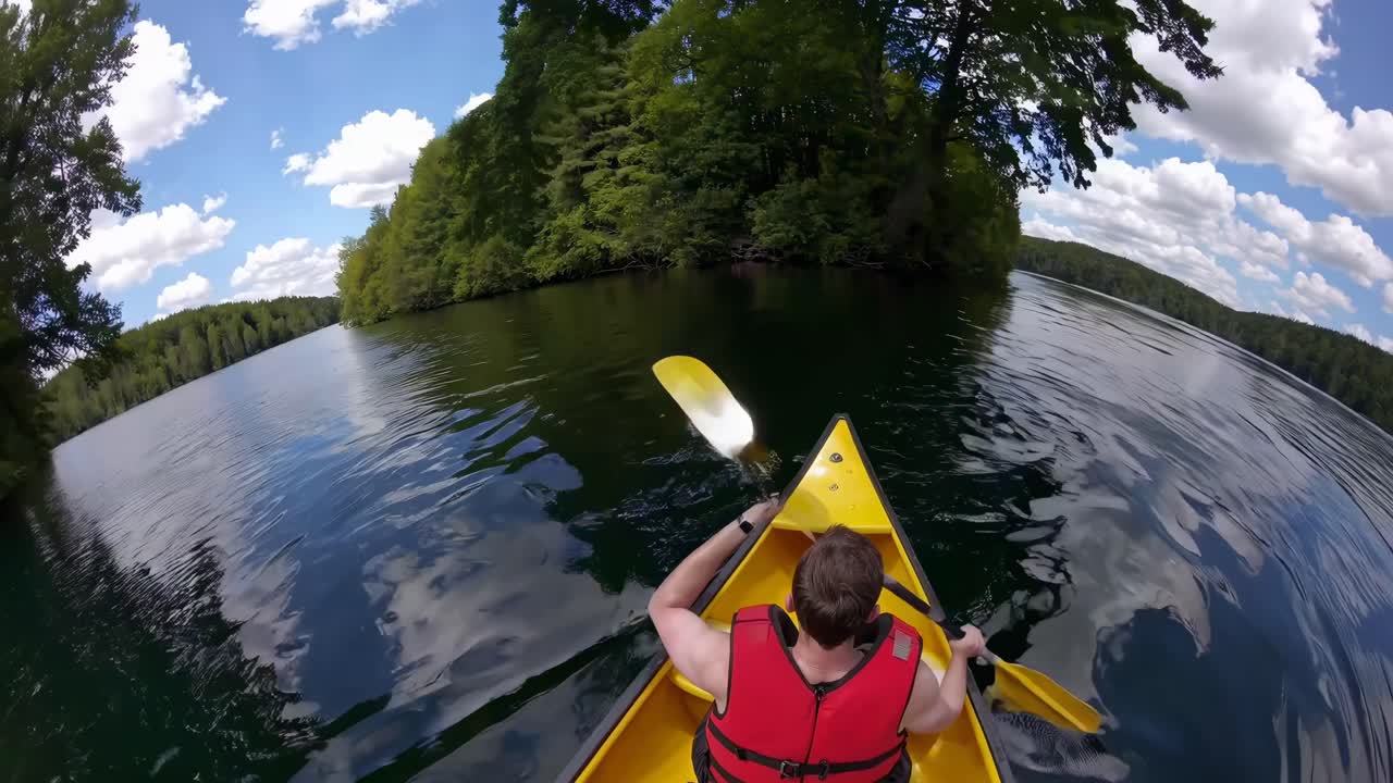 Video POV ripreso dall'alto, che mostra una persona in kayak su un lago sereno sotto un cielo azzurro brillante.