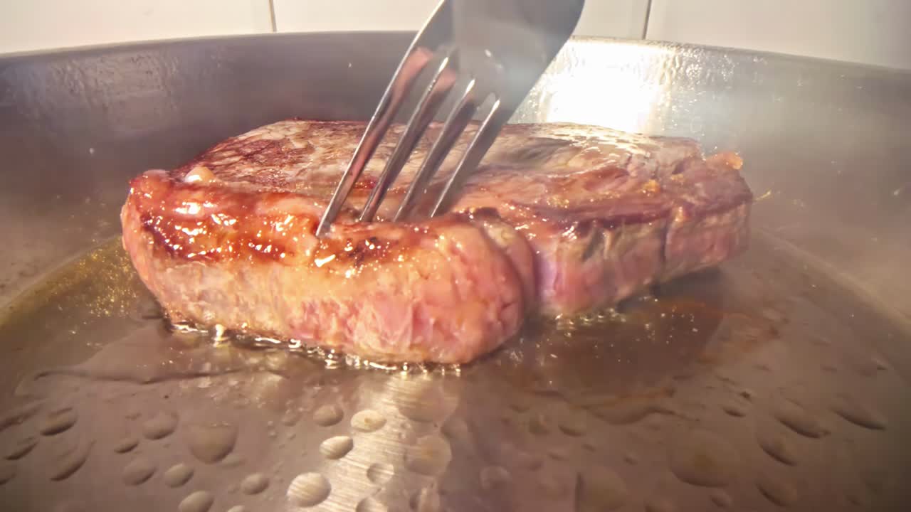 Braciola di maiale sfrigolante girata in una padella d'acciaio inossidabile con una forchetta, primo piano
