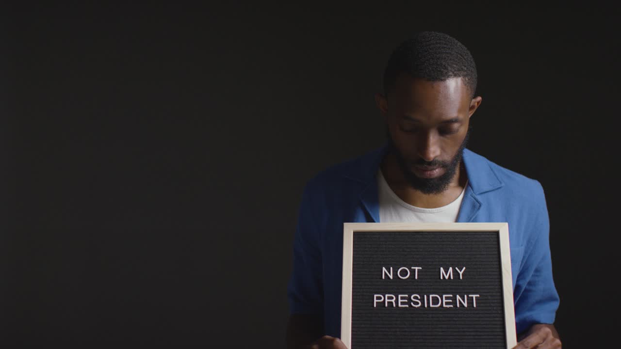 Portrait Of Man Holding Not My President Sign In Election Against Black Background