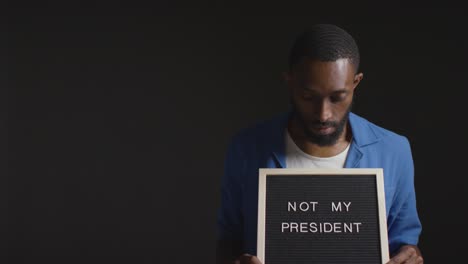 portrait of man holding not my president sign in election against black background