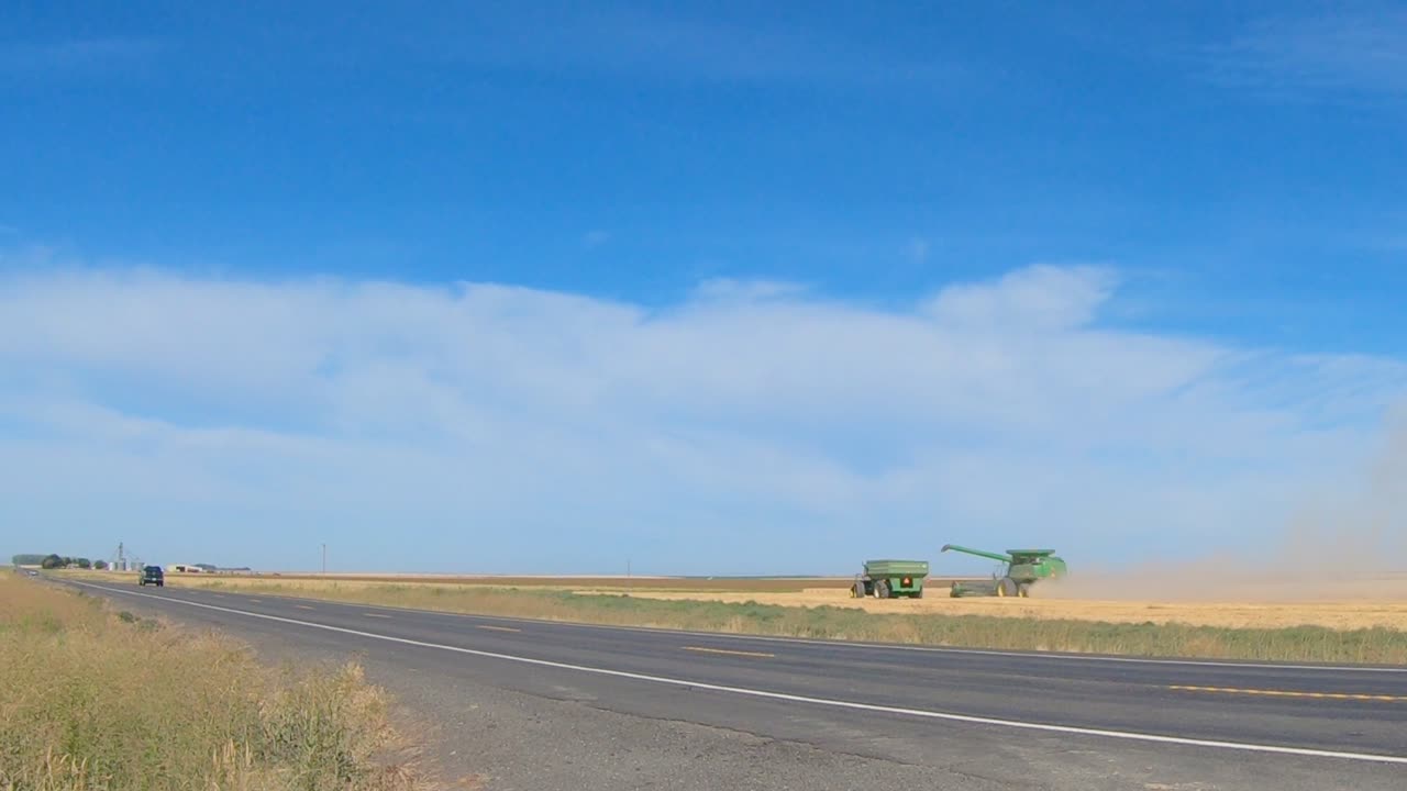 콤바인 수확기와 곡물 왜건은 동부 워싱턴 주에서 밀을 수확하고 있으며 교통량이 전경을 통과하고 있습니다.