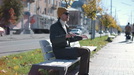 young blind man with smartphone sitting on bench in park in city, calling