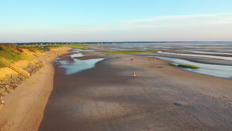 cape cod bay beach front houses aerial drone footage at low tide during golden hour with people walking, bright sun low and setting, pan right