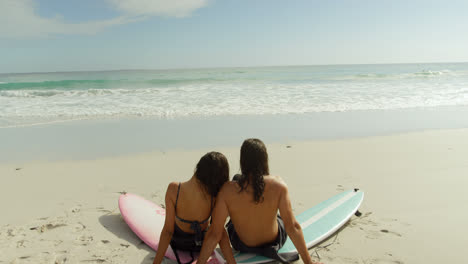 Surfer-couple-sitting-on-the-beach-with-surfboards-4K-4k