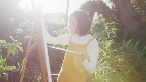 caucasian woman with brown hair painting in sunny garden