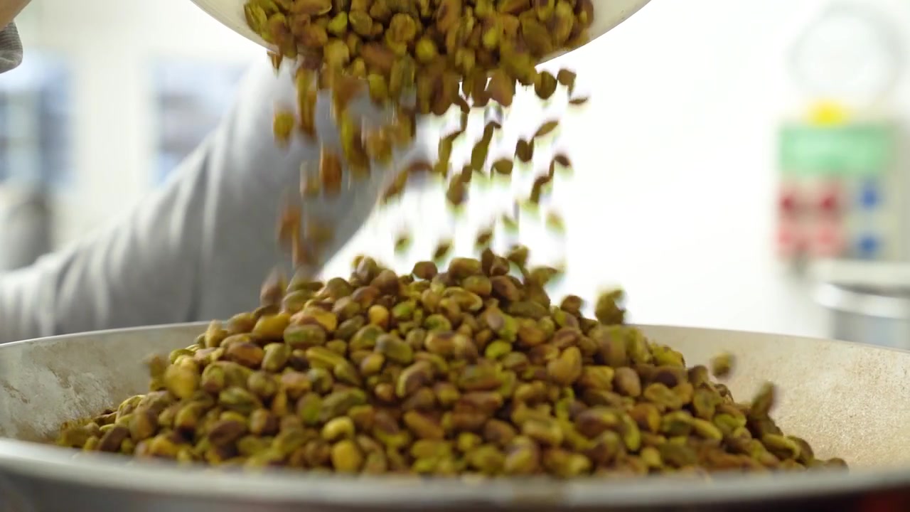 Pistachio nuts being poured into a large cooking pan in a professional kitchen environment