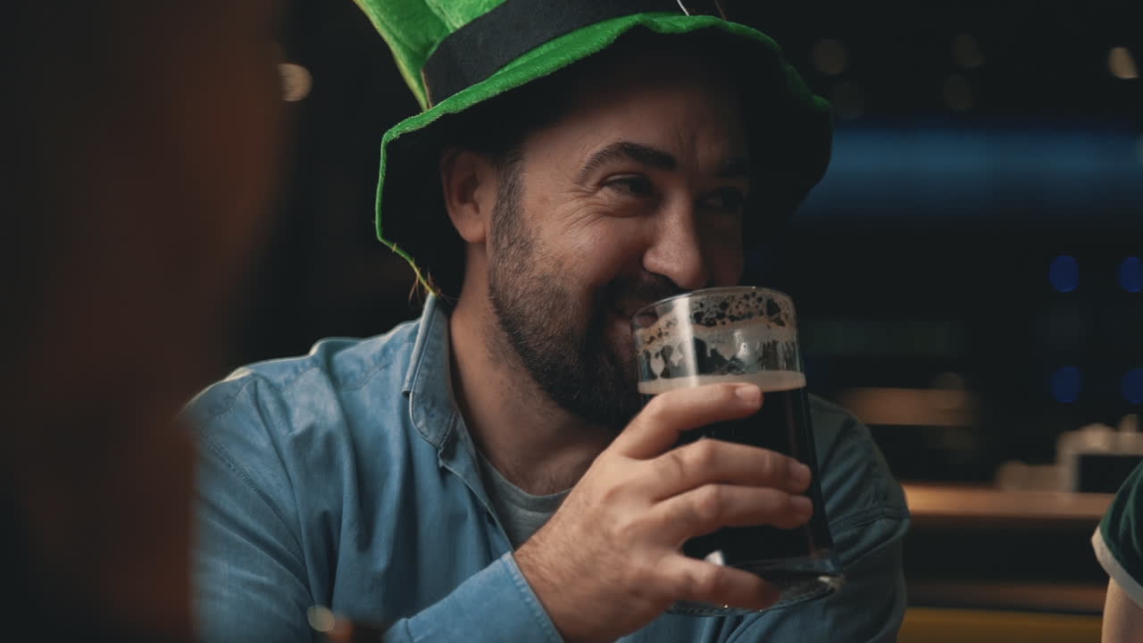 retrato de un hombre feliz con sombrero irlandés bebiendo una jarra de cerveza y hablando con amigos en un pub